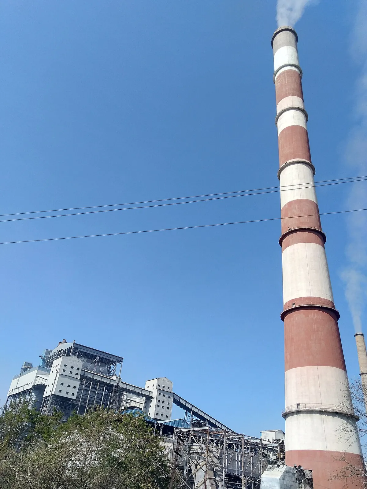 Chimney and boiler building of a thermal power plant in Chhattisgarh, India against a blue sky
